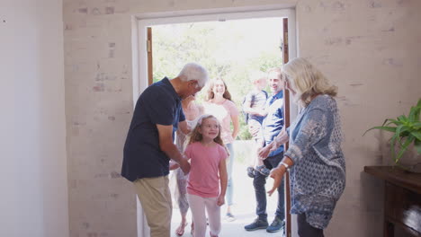 grandparents open front door of house to welcome multi-generation family on visit