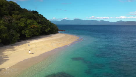 wide rotating drone shot of woman walking on nudey beach on fitzroy island