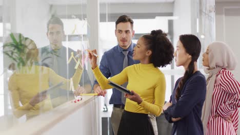 Group-of-diverse-business-people-taking-notes-on-glass-wall-and-talking-in-office,-slow-motion