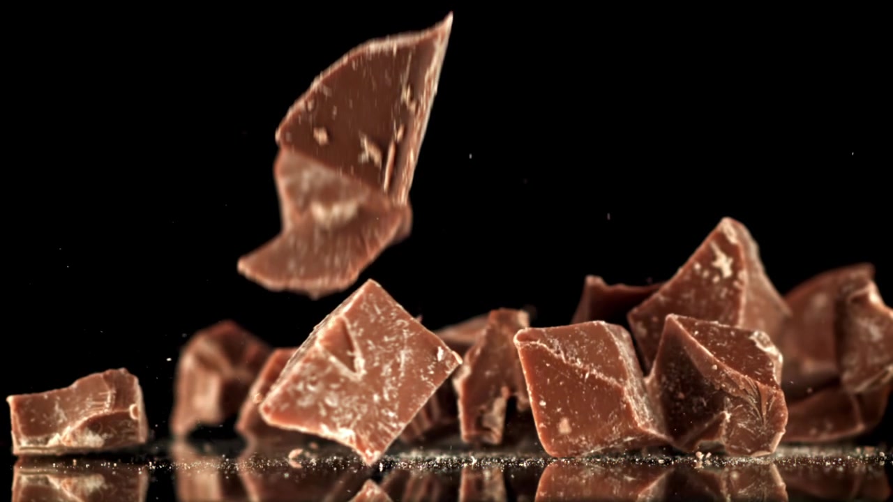 Pezzi di cioccolato che cadono e si disperdono su una superficie nera riflettente al rallentatore