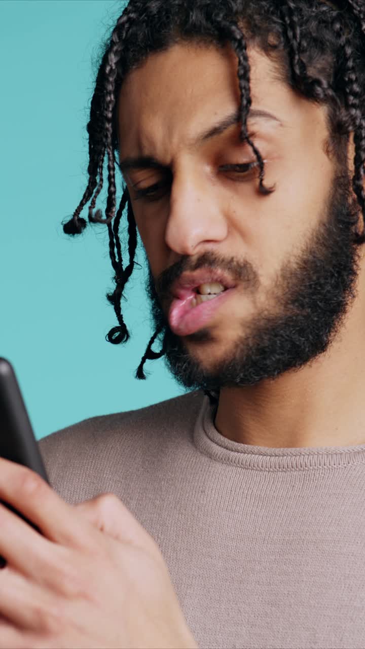 En mand optaget som vertikal video, der sms'er til en ven ved hjælp af en smartphone og griner af en sjov joke med en studieb baggrund