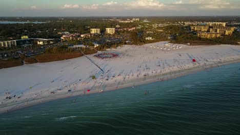 Toma-Aérea-De-Drones-Alejándose-De-La-Playa-De-Arena-Blanca-Con-Círculo-De-Tambores-En-Siesta-Key,-Florida-Al-Atardecer