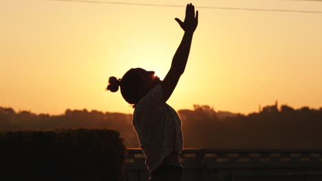 silhouette of young woman relaxing from yoga pose at sunrise in slow motion with a strong sun backlight. the sun shines between the silhouette with a beautiful flare