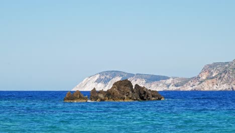 blue ocean with waves crashing on rocks in agia eleni beach, kefalonia, greece - wide shot