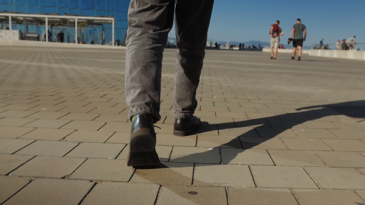 A man is seen ascending concrete stairs, with long shadows from sunlight on a striped pattern cast on the steps