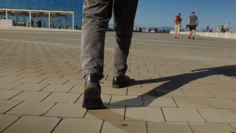 a man is seen ascending concrete stairs, with long shadows from sunlight on a striped pattern cast on the steps