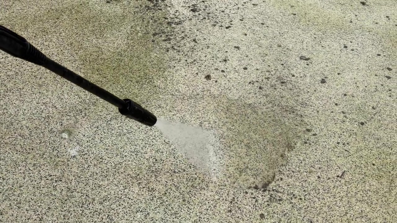 Primo piano di un'idropulitrice che rimuove alghe verdi e sporco dal pavimento in cemento di una piscina.