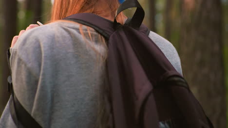 숲길을 따라 걸어가는 여자의 클로즈업, 배경에는 높은 나무가 있고, 어깨에 검은 가방을 흔들고, 긴 머리카락이 등 아래로 떨어집니다.