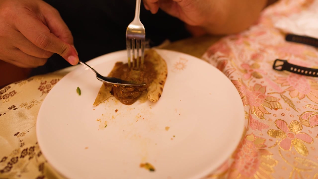 Detail rukou jedících příborem tradiční indické kari na plackách v restauraci.