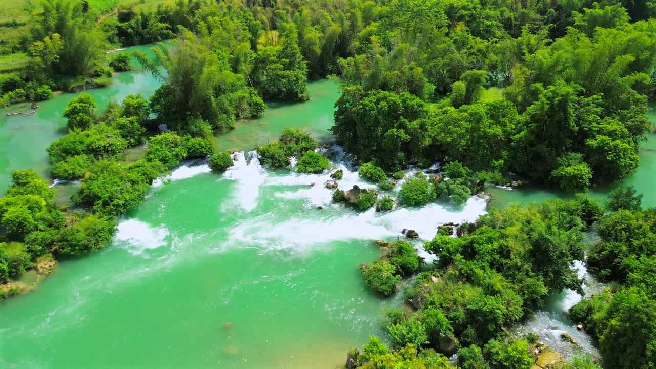 Ripresa drammatica con drone che mostra l'acqua turchese vibrante di un fiume che scorre attraverso piccole cascate e una fitta vegetazione tropicale verde in un paesaggio rurale