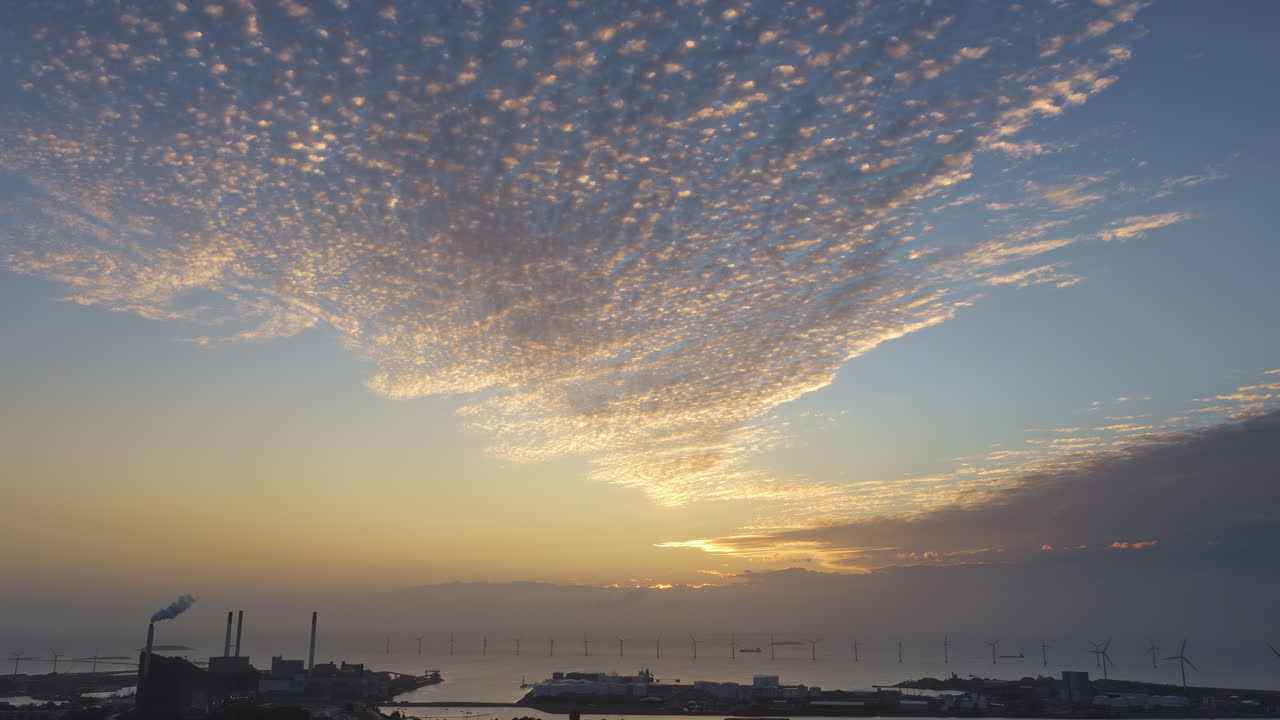 Aerial drone view of Copenhagen, Denmark at sunset with glowing skies, wind turbines in the background