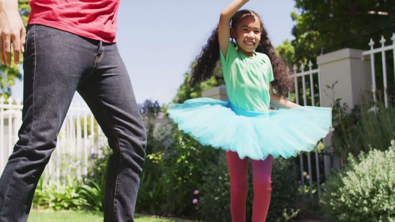 padre y hija biraciales felices bailando juntos en el jardín