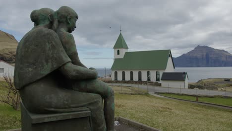 Wide-Pan-Right-of-a-Memorial-Statue-and-Church-in-Gjogv,-Faroe-Islands