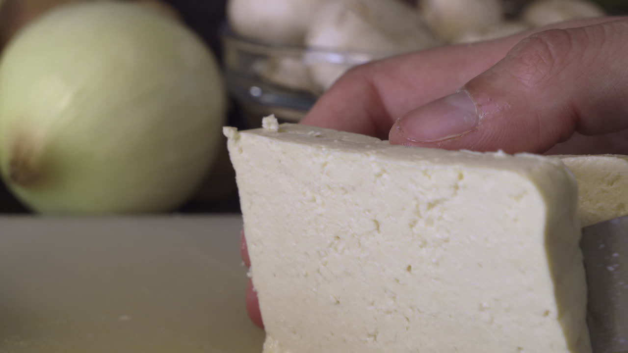 Slicing Uncooked Tofu With A Sharp Knife In The Kitchen - closeup shot