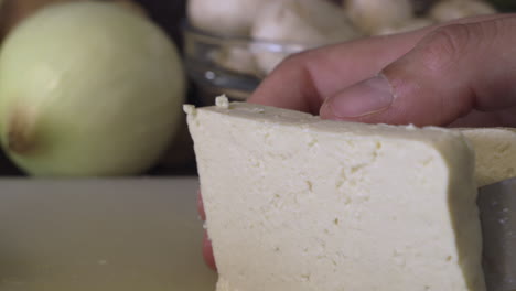 slicing uncooked tofu with a sharp knife in the kitchen - closeup shot