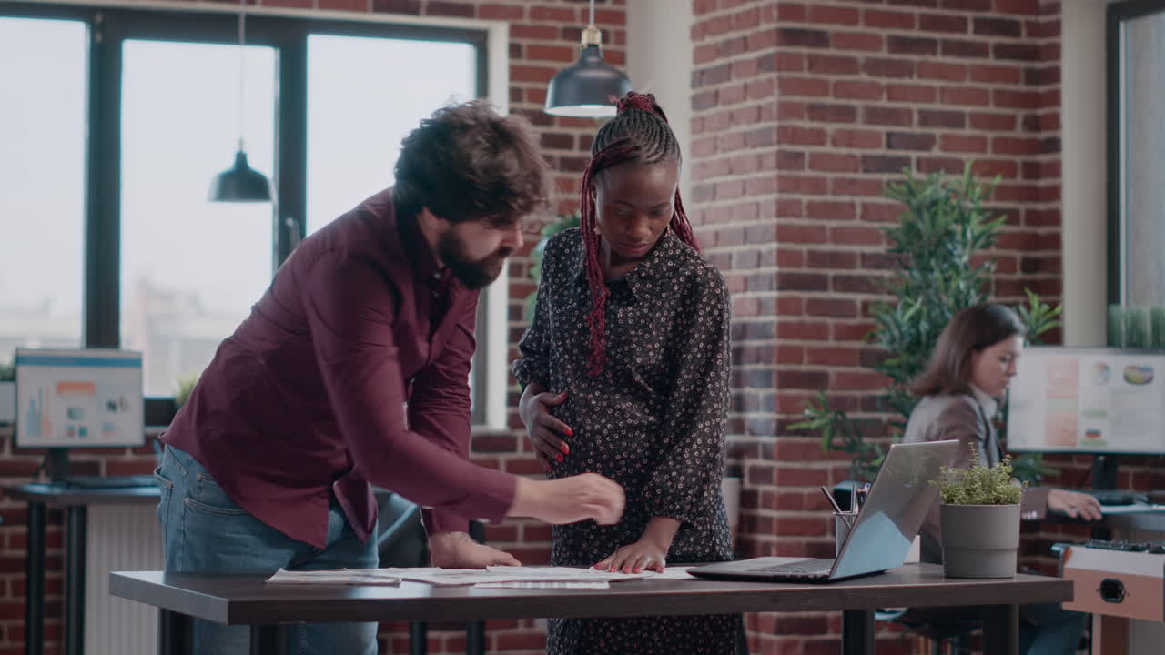 Woman expecting baby and working on business project with colleague