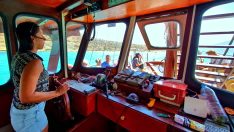 profile view of a woman handling the helm of a local tourist ship heading towards spinalonga fortress in crete, greece.