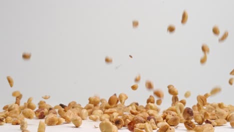 Chopped-salty-roasted-peanut-pieces-falling-onto-white-table-top-and-bouncing-into-a-pile-in-slow-motion