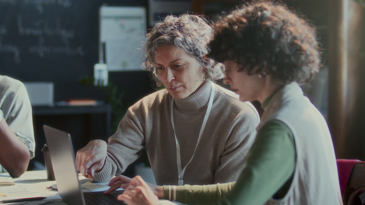 Teacher and Female Student Discussing Information on Laptop during Lesson