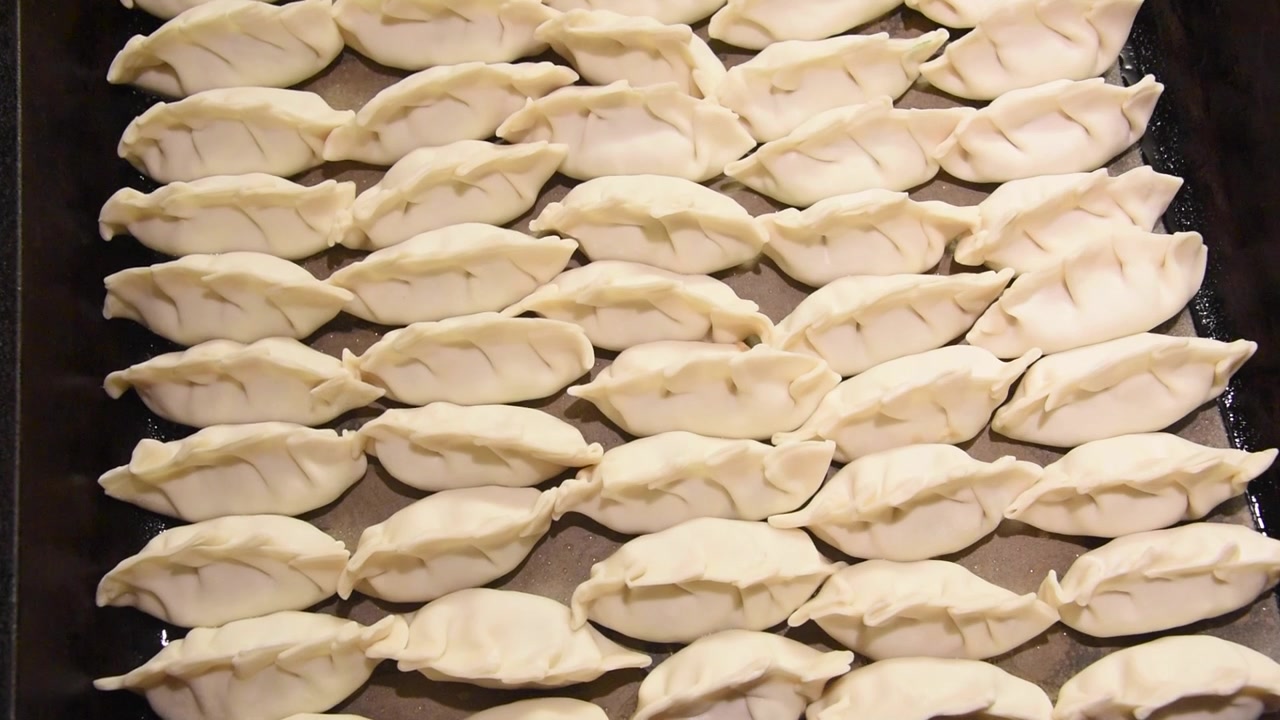 Fileiras de guiozas japoneses crus fritando em uma frigideira quente. Vista em close-up do prato asiático caseiro tradicional chiando no óleo