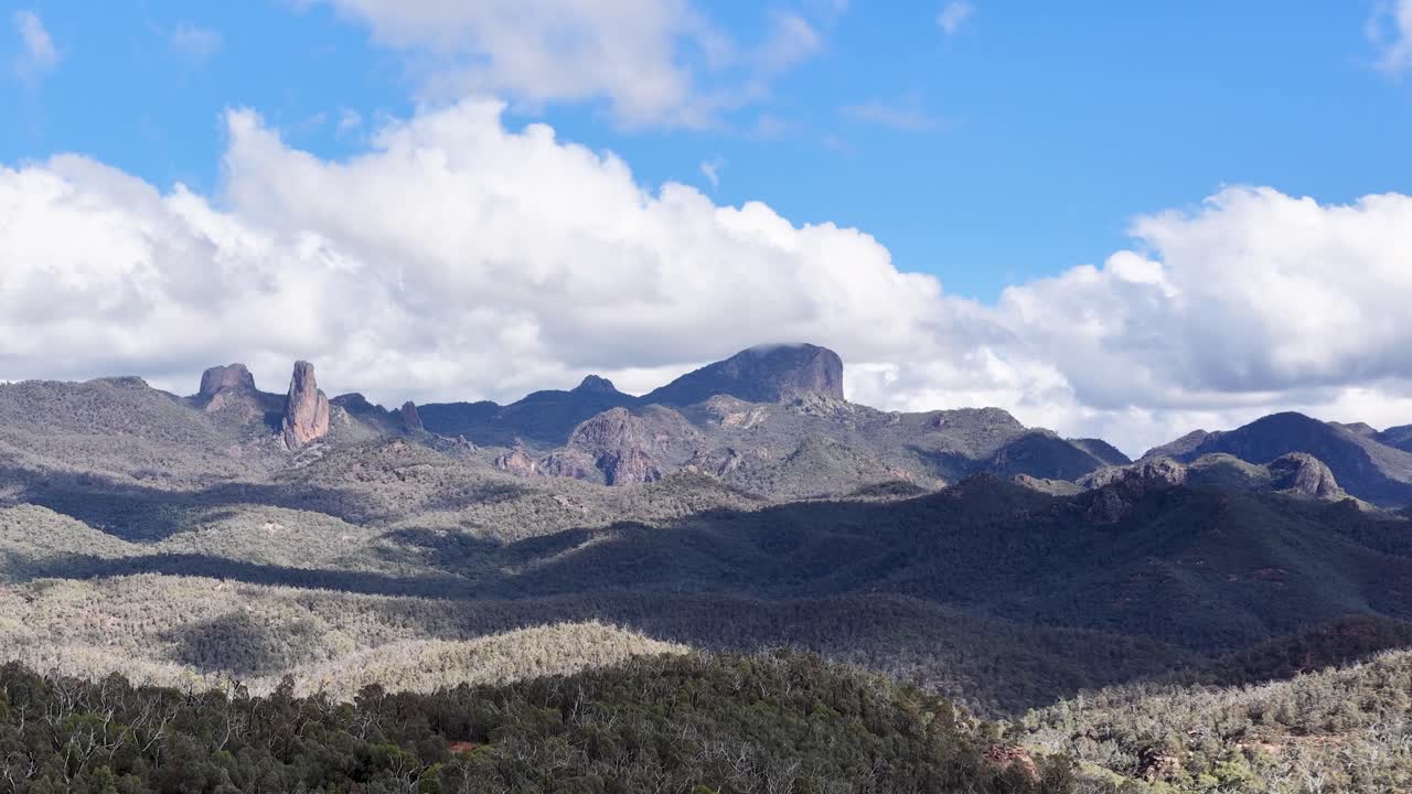 A daylight time-lapse pans smoothly across rugged mountains and forested hills under a blue sky with scattered clouds in Coonabarabran, New South Wales