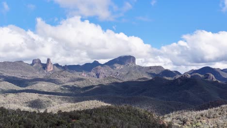 a daylight time-lapse pans smoothly across rugged mountains and forested hills under a blue sky with scattered clouds in coonabarabran, new south wales