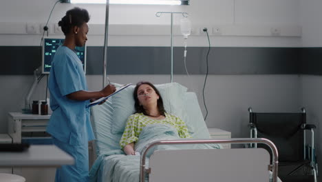 afro american asisstant checking sick woman while sitting in bed in hospital ward