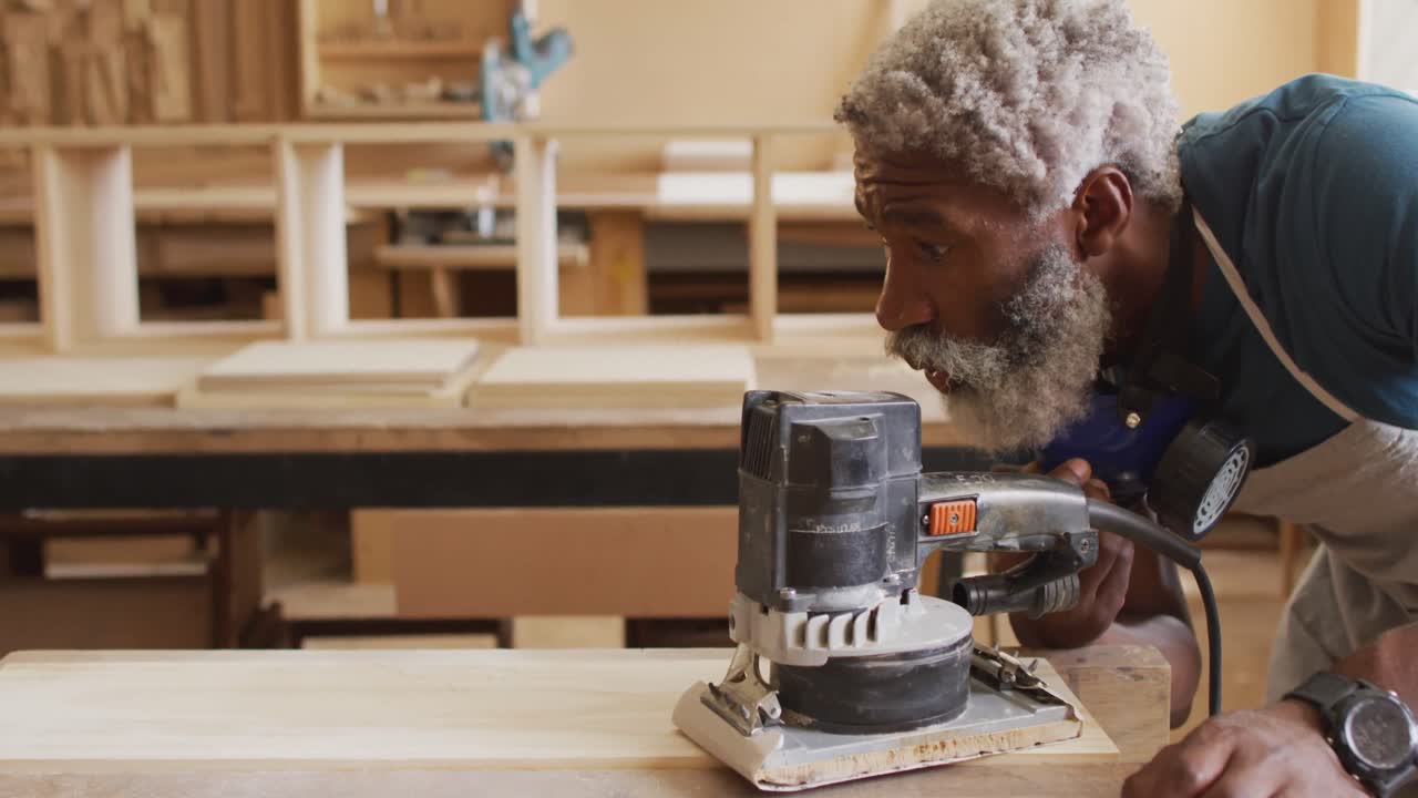 carpintero afroamericano que usa un molinillo eléctrico para moler tablas de madera en una carpintería