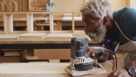carpintero afroamericano que usa un molinillo eléctrico para moler tablas de madera en una carpintería