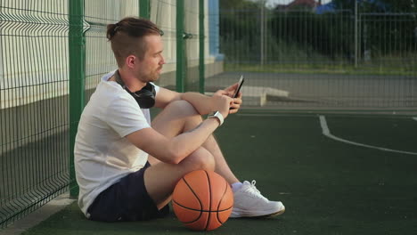 hombre relajándose en una cancha de baloncesto con un teléfono inteligente
