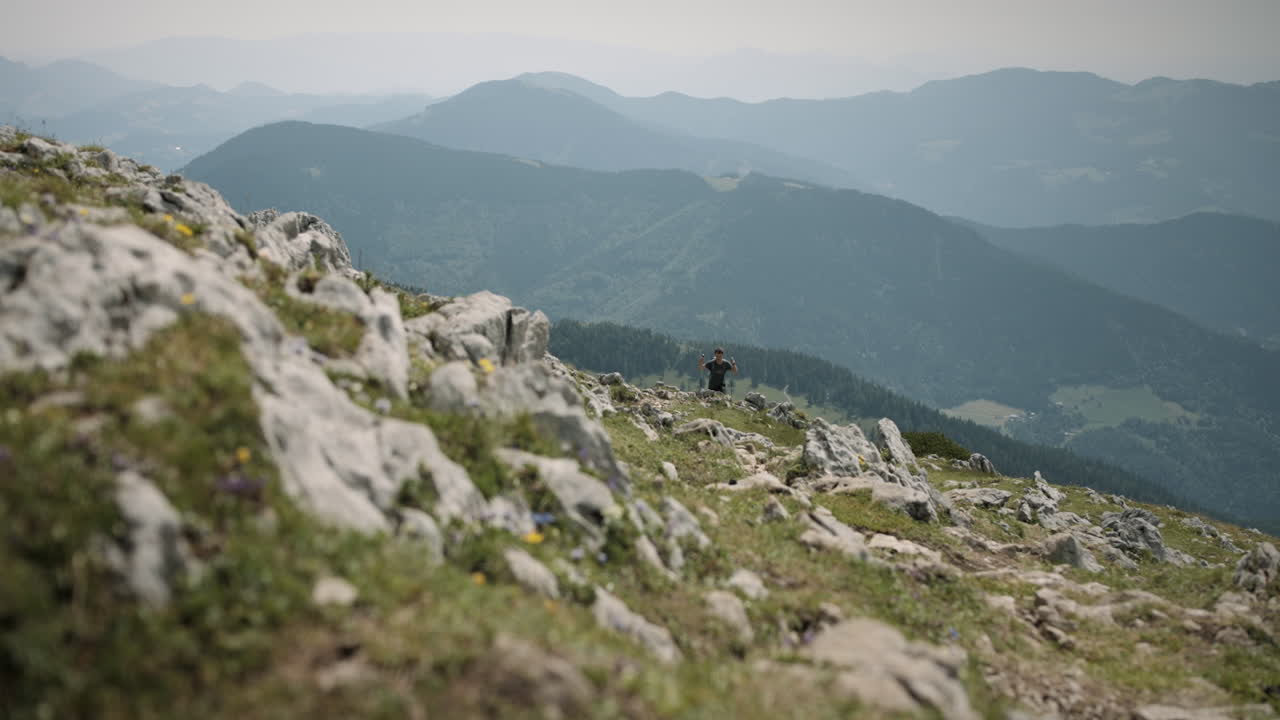 excursionista caminando escalando una montaña con bastones de senderismo, él es un valle y montañas cercanas parcialmente cubiertas de nubes delgadas