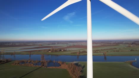 Langsames-Rotieren-Der-Turbinenblätter-Von-Windmühlen-In-Den-Niederlanden-Teil-Der-Nachhaltigen-Industrie-In-Der-Holländischen-Landschaft-Mit-Dem-Fluss-Ijssel-Tal-Im-Hintergrund-An-Einem-Sonnigen-Tag