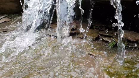 flowing-waterfall-from-a-mountain-spring-stream-running-down-huge-sandstone-slabs-of-rock-with-green-moss,-crystal-clear-drinking-water,-meditate-tranquil-and-peaceful-calm-slow-motion-footage