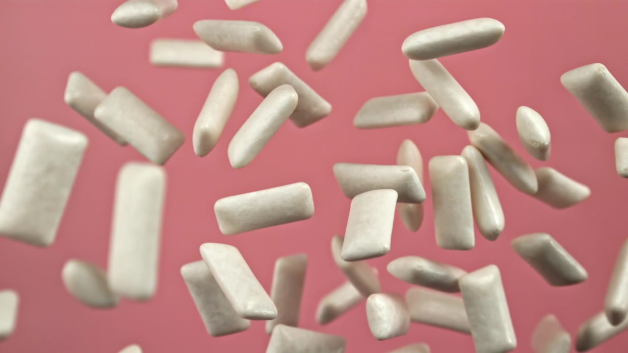 Pezzi di gomma da masticare bianchi che cadono al rallentatore su sfondo rosa.