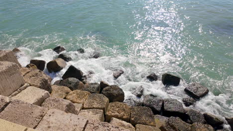 las olas iluminadas por el sol chocan contra los bloques rocosos de rompeolas bajo un cielo despejado