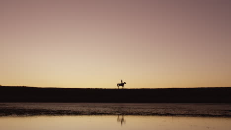 a silhouetted woman riding a horse on a ranch