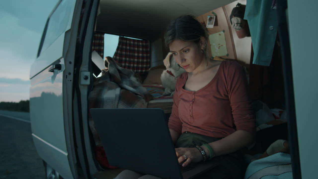 mujer sentada en una furgoneta con perro y usando una computadora portátil