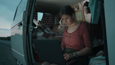 Woman-Sitting-in-Camper-Van-with-Dog-and-Using-Laptop