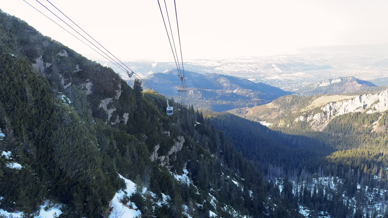 A snowy valley between mountain peaks with forest shadows and golden afternoon light, rearview out of tram gondola