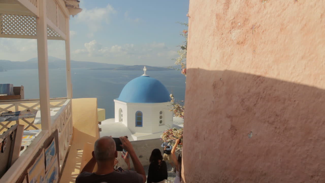 los turistas caminan y toman fotografías de la famosa capilla de la cúpula azul con vistas a la caldera en oia santorini