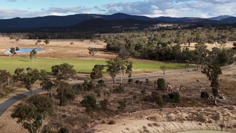 aerial camera slowly pans across a rural landscape with farmland, trees, a dam, and distant mountains under partly cloudy daylight in stanthorpe, queensland