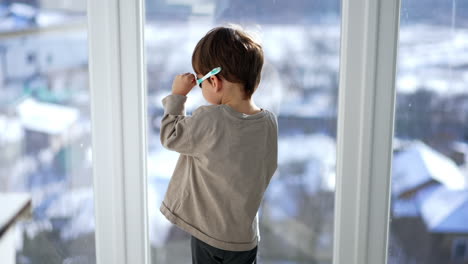 baby boy stands at the window wearing the sunglasses. kid turns to camera and points at the window.