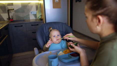 giving healthy food to a little infant. mother feeds some fresh avocado to her son.
