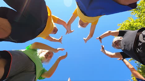 view from below of a senior football team standing in circle, whooping, raising arms up and clapping hands