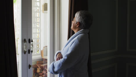 Senior-mixed-race-woman-at-home-looking-out-of-windows