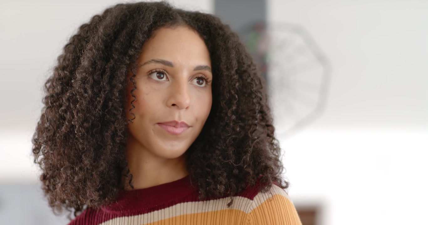 Obiettivo inclinato verso l'alto, che mostra una donna afroamericana adulta in cucina con un maglione a righe, sguardo attento
