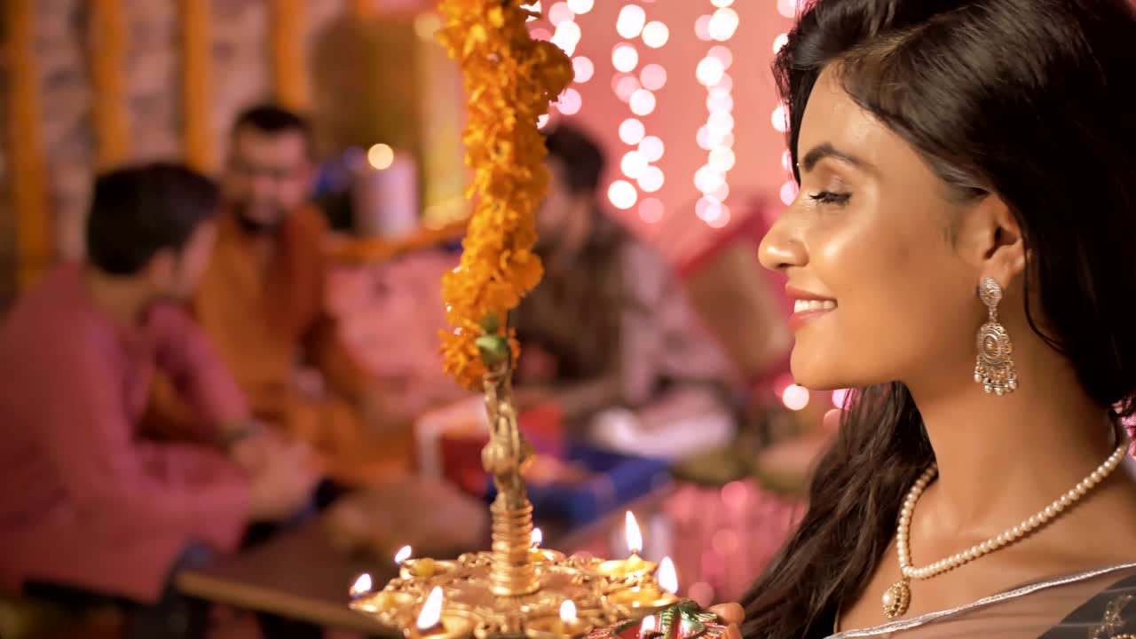 traditional woman lighting a oil lamp during Diwali festival while her family members talking in the background.