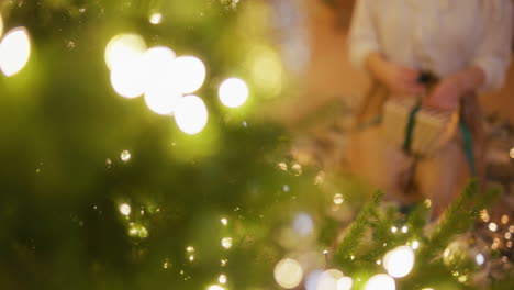 primer plano de las manos de una mujer envolviendo regalos por un árbol de navidad decorado
