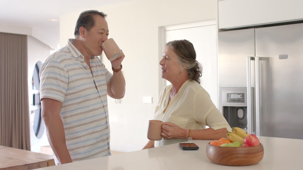 Senior couple drinking coffee and talking in modern kitchen with fruit bowl