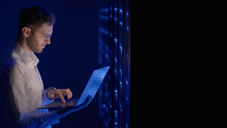 Face-portrait-of-man-working-in-server-room-with-laptop.-technician-doing-a-checkup-in-the-server-room.-Caucasian-engineer-wearing-grey-worker-jacket